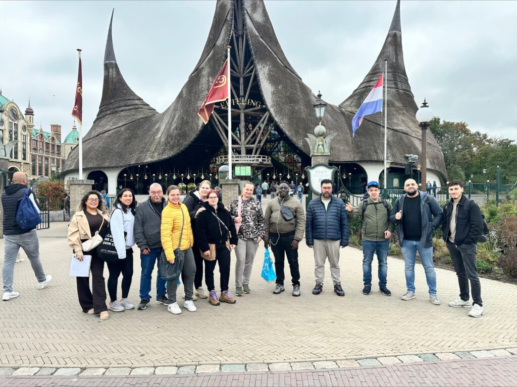 12 bewoners en begeleiders op een rij voor de ingang van de Efteling. Achter hen een rode vlag met gele letters en gebouw met strooien dak en 'De Efteling'